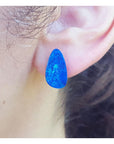 A close-up view of a doublet blue opal stud earring worn on an ear.