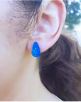 Pear-shaped Australian opal doublet earring in deep blue-green flashing colors on an ear.