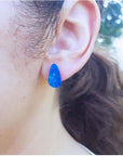 Pear-shaped Australian opal doublet earring in deep blue-green flashing colors on an ear.