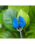 Matching pair of pear-shaped Australian opal doublets with deep blue-green flash, held by tweezers on green leaves.