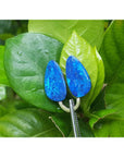 Matching pair of pear-shaped Australian opal doublets with deep blue-green flash, held by tweezers on green leaves.