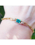 14k gold paperclip bracelet with a natural colombian emerald and accent diamonds on a wrist.