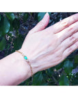 Paper clip bracelet in 14K yellow gold with a natural emerald and diamonds on a woman's wrist.