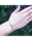 Paper clip bracelet in 14K yellow gold with a natural emerald and diamonds on a woman's wrist.