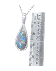 Teardrop-shaped opal pendant on a white gold chain with a ruler for scale on a white background.