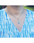 A lady wearing a blue and white patterned top with a necklace featuring a teardrop-shaped opal pendant.