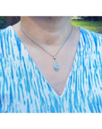 A lady wearing a blue and white patterned top with a necklace featuring a teardrop-shaped opal pendant.