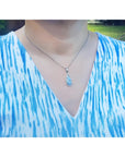 Pear-shaped Australian opal pendant with halo diamonds on an 18K white gold chain, worn on a person.