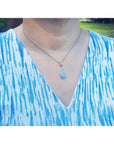 Pear-shaped Australian opal pendant with halo diamonds on an 18K white gold chain, worn on a person.