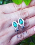 Teardrop-shaped earrings with colombian emeralds held on a hand against a blurred green background