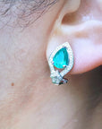 Close-up of an ear wearing clip/post emerald teardrop earring with a blurred natural background