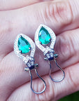 Pair of emerald teardrop earrings held between fingers displaying clip system.
