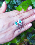 Hand holding a pair of earrings with natural emeralds against a leafy background