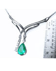 14K white gold necklace with a pear-shaped emerald and diamond chevron design, shown with a ruler.