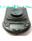 1.74-carat pear-cut Colombian emerald on a digital scale, with other emeralds in the background.