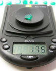 1.74-carat pear-cut Colombian emerald on a digital scale, with other emeralds in the background.