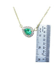 Emerald pear-shaped necklace with diamond halo on 14K yellow gold chain, next to a ruler for scale.