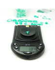1.84 carat pear-cut natural Muzo Colombian emerald on a digital scale, surrounded by other green emeralds.
