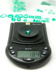 1.84 carat pear-cut natural Muzo Colombian emerald on a digital scale, surrounded by other green emeralds.