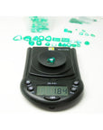 1.84 carat pear-cut natural Muzo Colombian emerald on a digital scale, surrounded by other green emeralds.