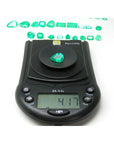 4.17 ct pear-cut natural Muzo Colombian emerald on a digital scale, with other emeralds in the background.