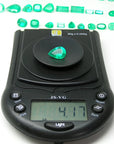 4.17 ct pear-cut natural Muzo Colombian emerald on a digital scale, with other emeralds in the background.