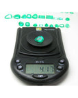 4.17 ct pear-cut natural Muzo Colombian emerald on a digital scale, with other emeralds in the background.