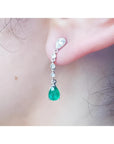 Close-up of a natural colombian emerald teardrop earring in white gold on a person's ear.