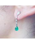 Close-up of a natural colombian emerald teardrop earring in white gold on a person's ear.
