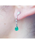 Close-up of a natural colombian emerald teardrop earring in white gold on a person's ear.