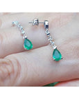 14K white gold pear-shaped emerald drop earrings with brilliant white diamond accents.