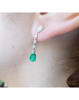 14K white gold pear-shaped emerald drop earring with brilliant white diamonds on an ear.
