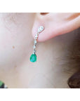14K white gold pear-shaped emerald drop earring with brilliant white diamonds on an ear.
