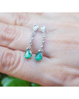 Natural teardrop emerald earrings with diamond accent on a hand.