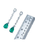 1.05 ct. pear-shaped emerald drop earrings in 14K white gold with diamonds, next to a ruler.