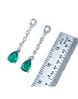 1.05 ct. pear-shaped emerald drop earrings in 14K white gold with diamonds, next to a ruler.