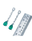 1.05 ct. pear-shaped emerald drop earrings in 14K white gold with diamonds, next to a ruler.