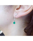 14K white gold pear-shaped emerald drop earrings with brilliant white diamonds on an ear.