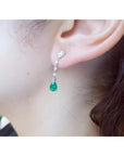 14K white gold pear-shaped emerald drop earrings with brilliant white diamonds on an ear.