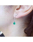 14K white gold pear-shaped emerald drop earrings with brilliant white diamonds on an ear.