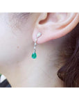 14K white gold pear-shaped emerald drop earrings with brilliant white diamonds on an ear.