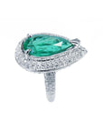 An emerald ring, top and right-side profile view pear shaped green gemstone held by three prong set, encircled by double halo diamond.