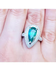 Ladies' ring with a pear-shaped natural colombian emerald in a halo diamond on a person's finger.