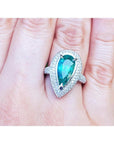 Ladies' ring with a pear-shaped natural colombian emerald in a halo diamond on a person's finger.