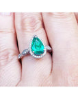 1.43 ct teardrop emerald engagement ring in 14K white gold with diamond halo and twisted band on a hand.