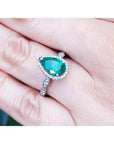 1.43 ct teardrop emerald engagement ring in 14K white gold with diamond halo and accents on a hand.