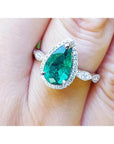 Pear cut natural emerald ring with a halo diamond in 14k white gold on a finger.
