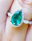 Pear cut emerald ring with a halo diamond in white gold on a finger.