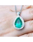 Green teardrop emerald gemstone pendant on a white gold chain held between fingers.
