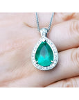 Pear-shaped emerald pendant with halo diamonds in 14K white gold, held by a hand.